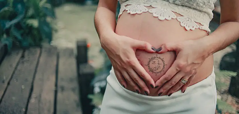 Donna incinta che mostra il suo tatuaggio sole e luna sul pancione