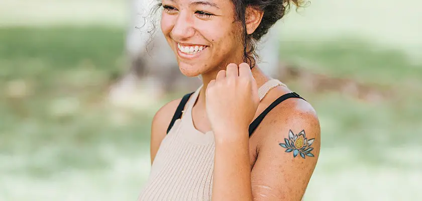 Ragazza sorridente con tatuaggio a fiore di loto sul braccio sinistro - Tatuaggi piccoli con significato