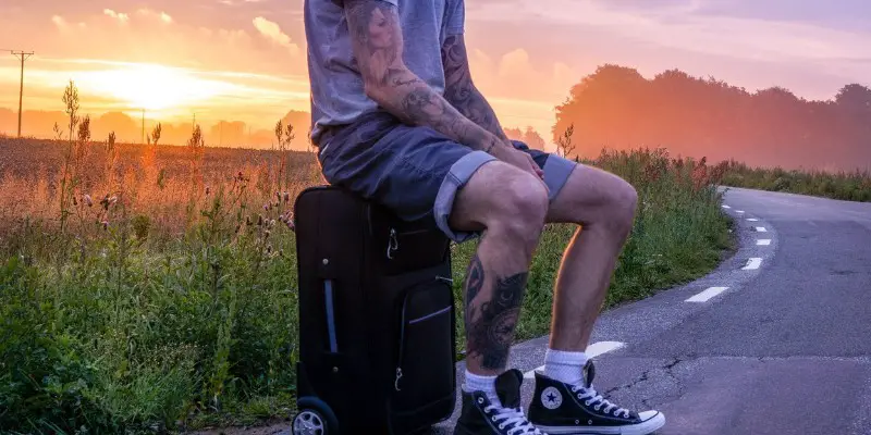Ragazzo con i tatuaggi seduto sulla valigia