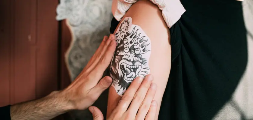 Tatuatore che posiziona un adesivo sul braccio destro del suo cliente