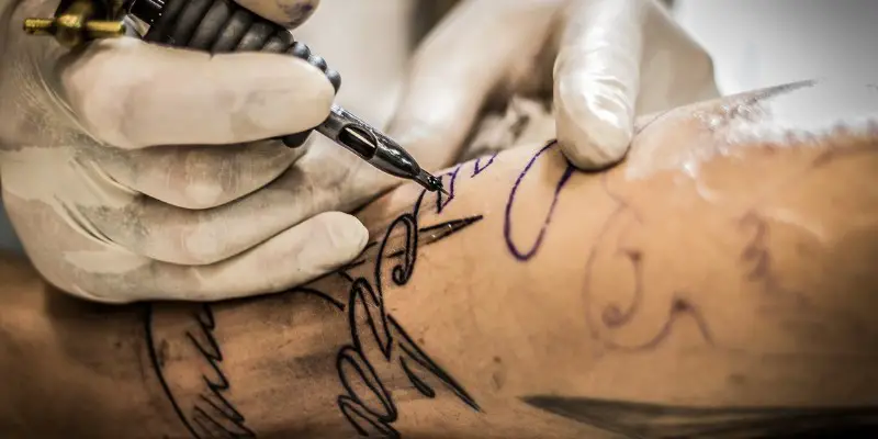 Tatuatore con guanti in lattice che effettua un tatuaggio sul braccio