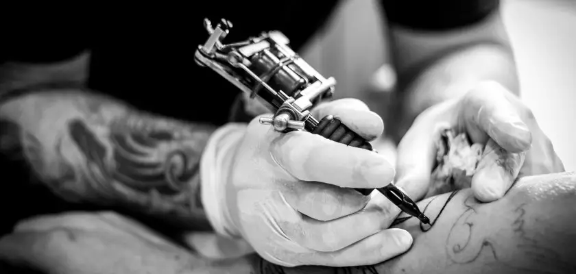 Tatuatore che effettua uno dei tatuaggi piccoli scelti dal cliente sul suo braccio