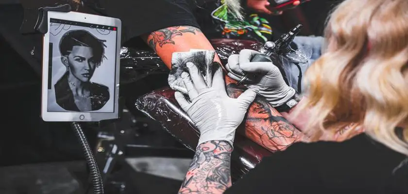 Tatuatore donna che effettua un tatuaggio sul braccio destro della sua cliente