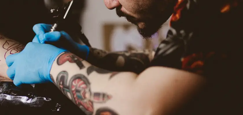 Tatuatore professionista che sta realizzando uno dei tatuaggi braccio scelti dal cliente sul suo braccio destro