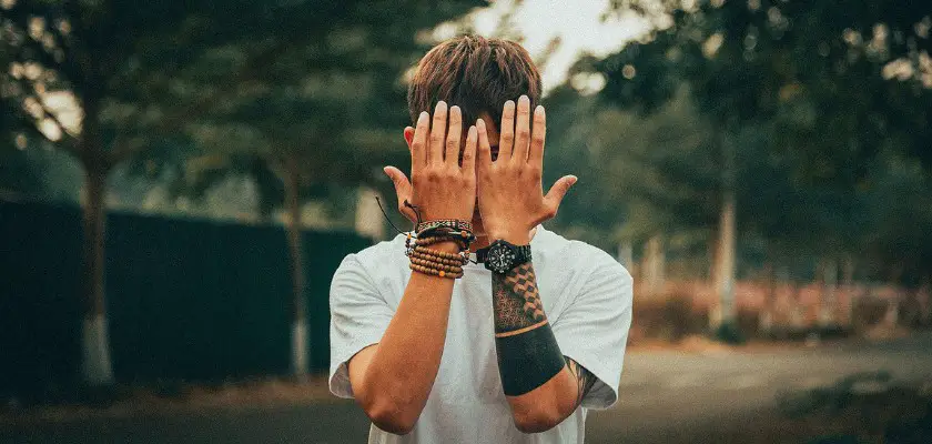 Ragazzo che si copre il volto per mostrare i suoi tatuaggi sulle braccia