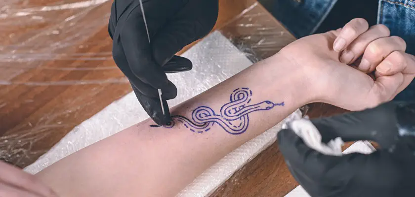 Tatuatore che effettua un tatuaggio sul braccio destro della sua cliente – Ogni quanto lavare il tatuaggio