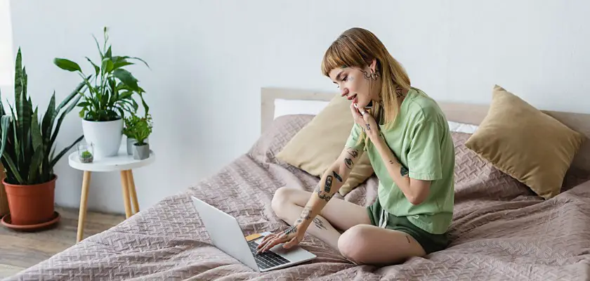 Bella ragazza bionda distesa sopra le coperte del letto con la mano sinistra appoggiata sulla tastiera del Notebook