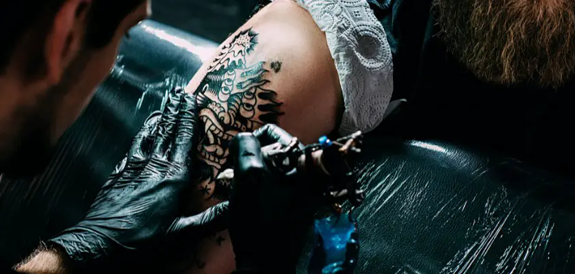 Tatuatore professionista che sta effettuando un tatuaggio sul braccio destro del suo cliente barbuto – Dopo quanto posso esporre il tatuaggio al sole