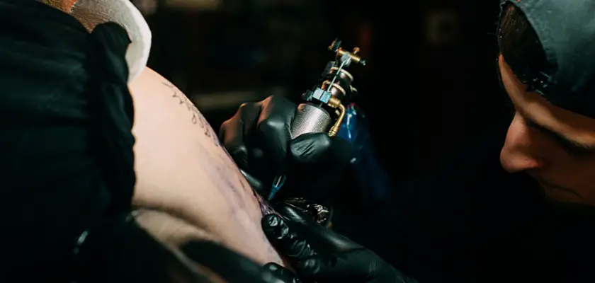 Vista parziale di un tatuatore professionista mentre sta effettuando un tatuaggio sul braccio del suo cliente