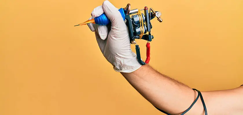 Vista parziale di un uomo con il braccio destro disteso mentre tiene in mano una macchinetta per tatuaggi