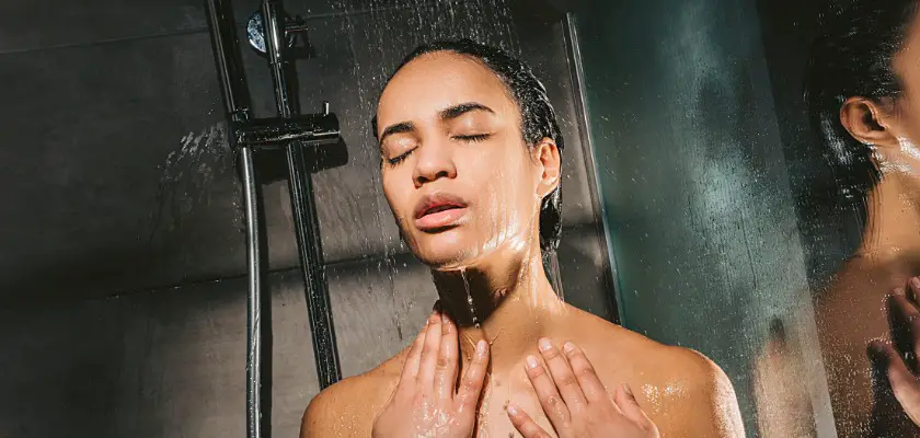 Attraente donna afro-americana con gli occhi chiusi mentre si fa scorrere l’acqua dal telefono della doccia – Si può fare la doccia con il tatuaggio appena fatto