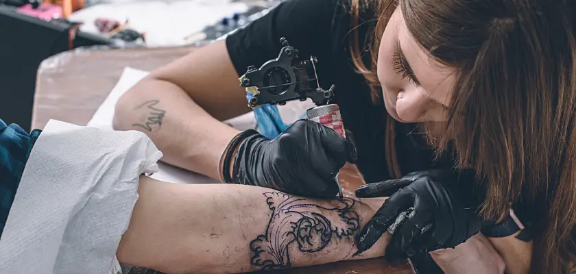 Vista di un tatuatore donna mentre effettua un tatuaggio sul braccio destro del suo cliente nel suo studio