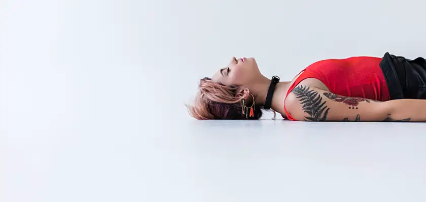 Vista laterale parziale di una ragazza attraente tatuata sdraiata a terra a pancia in su – Dopo quanto si toglie la pellicola dal tatuaggio