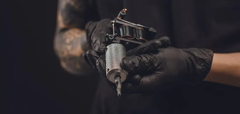 Vista parziale di un tatuatore professionista che tiene in mano la macchinetta per tatuaggi
