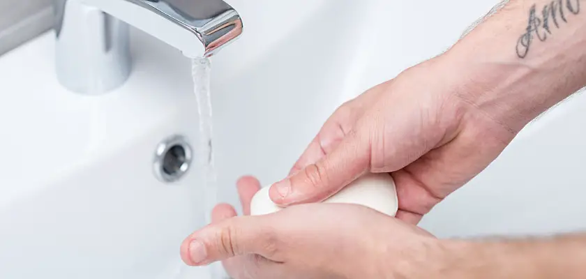 Vista parziale di un uomo che si lava le mani con il sapone mentre si fa scorrere l’acqua del lavandino in bagno – Come lavare il tatuaggio