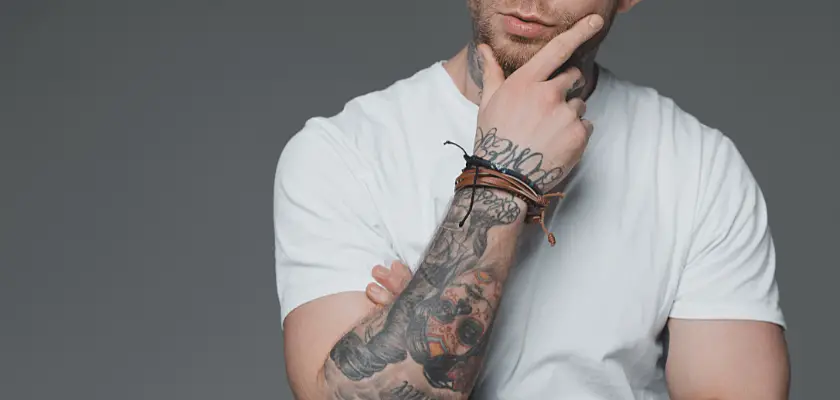 Colpo ritagliato di un giovane uomo tatuato con t-shirt e con una mano sul mento – Che tatuaggio fare