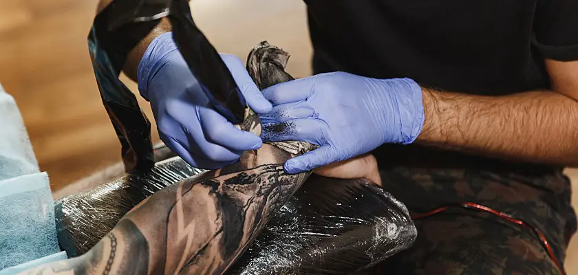 Primo piano di un tatuatore professionista che fa un tatuaggio sul braccio di un giovane cliente a macchina con inchiostro nero