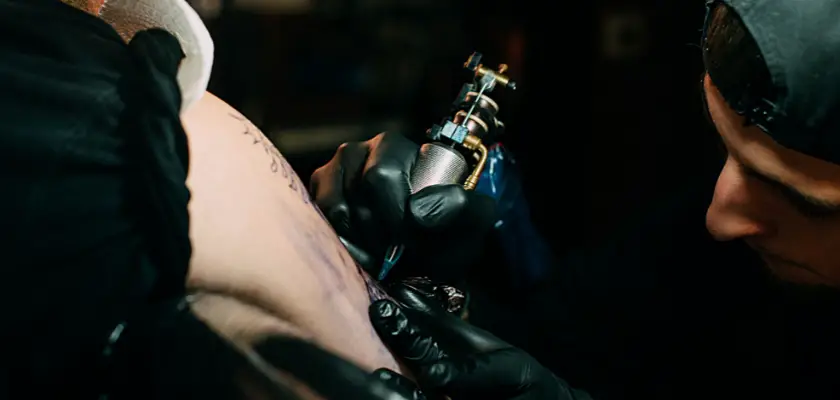 Tatuatore professionista mentre sta effettuando un tatuaggio chicano sul braccio del suo cliente