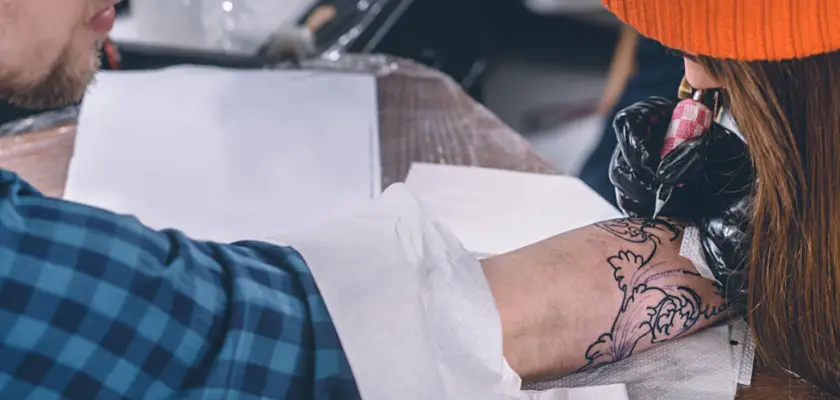 Vista parziale di un tatuatore donna mentre effettua uno dei tatuaggi estate scelti dal cliente sul suo braccio destro