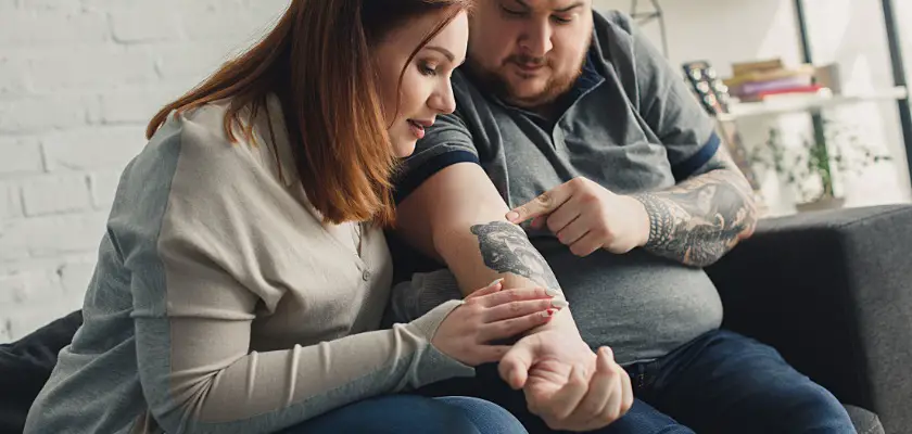 Fidanzato che mostra alla sua fidanzata il nuovo tatuaggio mentre sono seduti sul divano – Quando fare un tatuaggio