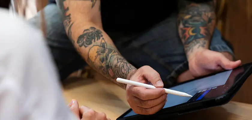 Tatuatore esperto che mostra uno dei tatuaggi temporanei che fanno al caso del cliente sul monitor del Tablet