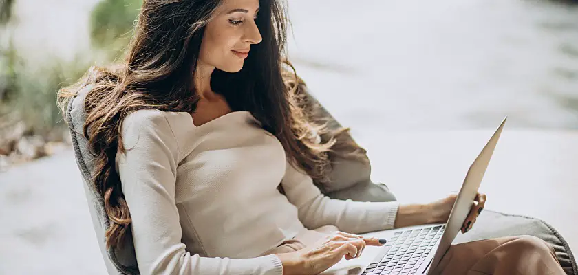 Vista laterale di una giovane donna d’affari allegra seduta in un cahir mentre lavora con il suo Laptop
